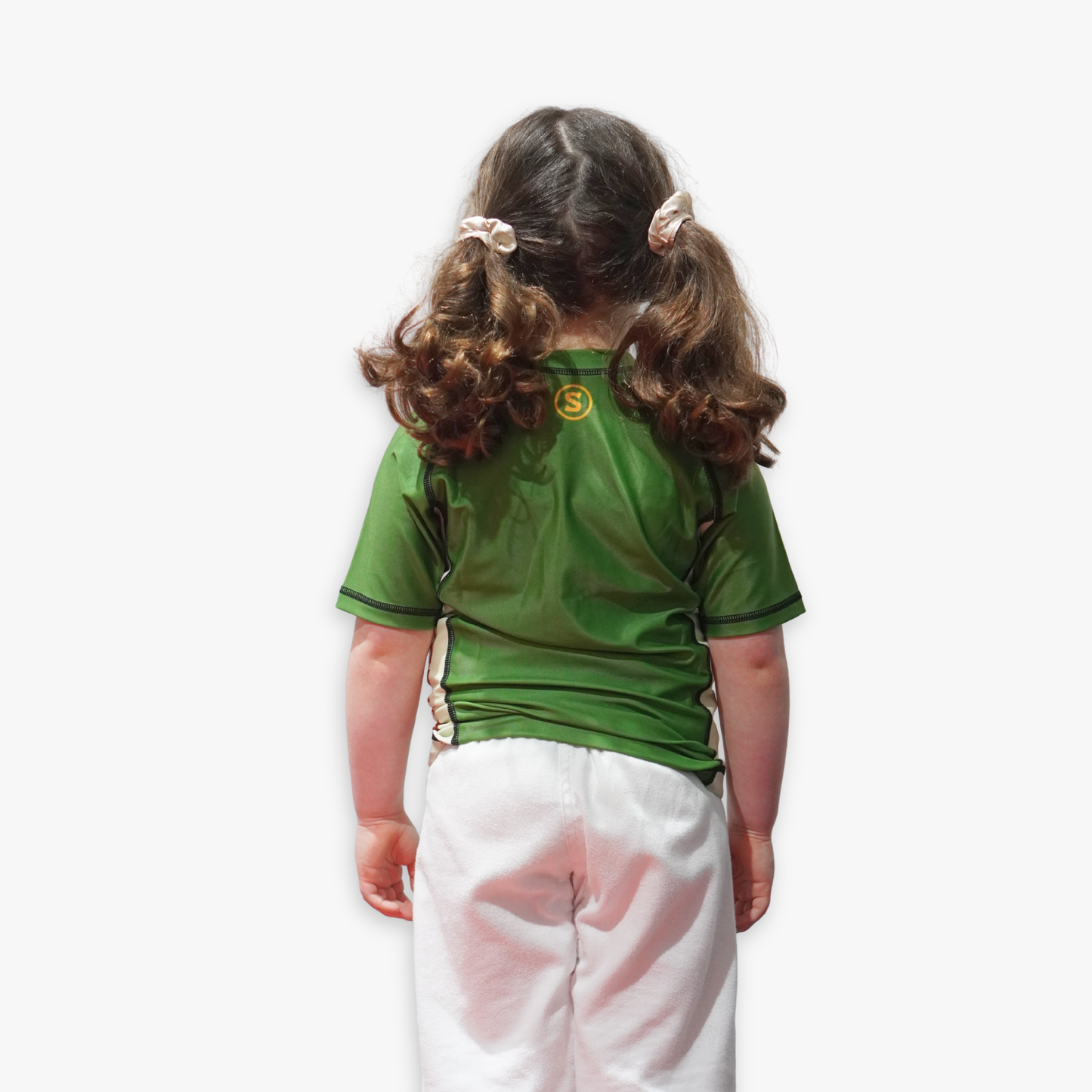 Child wearing a green Sunna rashguard on a white background facing a wall